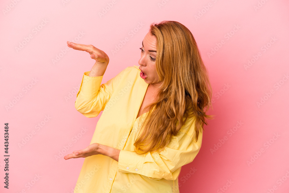 Caucasian blonde woman isolated on pink background shocked and amazed holding a copy space between hands. Caucasian blonde woman isolated on pink background shocked and amazed holding a copy space between hands.