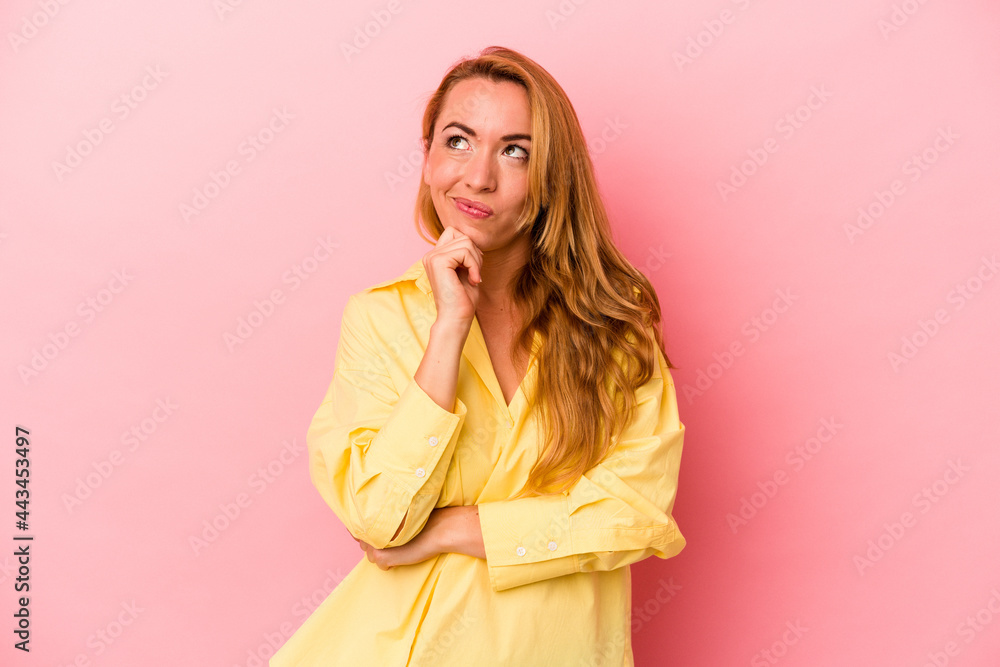 Caucasian blonde woman isolated on pink background relaxed thinking about something looking at a copy space. Caucasian blonde woman isolated on pink background relaxed thinking about something looking at a copy space.
