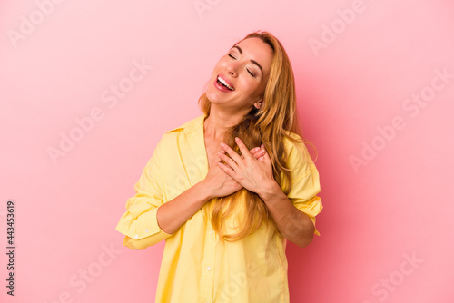 Caucasian blonde woman isolated on pink background has friendly expression, pressing palm to chest. Love concept. photo