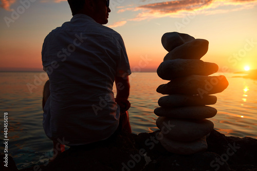 Canvas Print Silhouette of a man and zen stones on a ocean sea cliff in sunset sunrise time