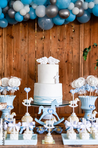 Decoração da mesa do bolo de festa de batismo e aniversário de menino com muitos doces diferentes, com tema de cavalinhos e anjinhos nas cores azul e branco. photo