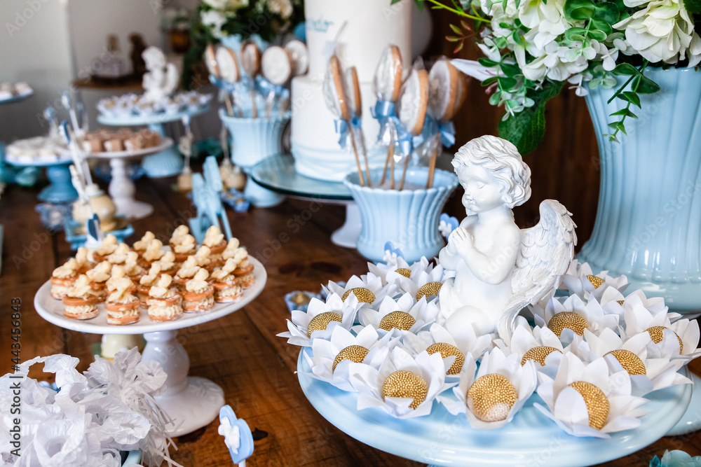 Decoração da mesa do bolo de festa de batismo e aniversário de menino com muitos doces diferentes, com tema de cavalinhos e anjinhos nas cores azul e branco.