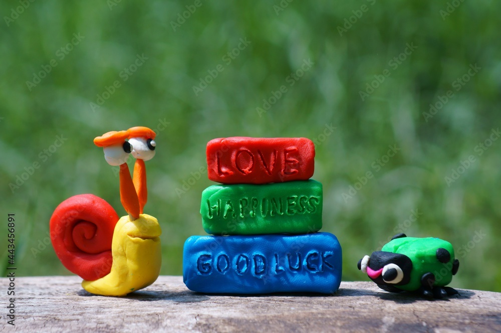 Fototapeta premium Toy snail and ladybug made of plasticine close-up. Next to the inscription love, happiness, good luck.