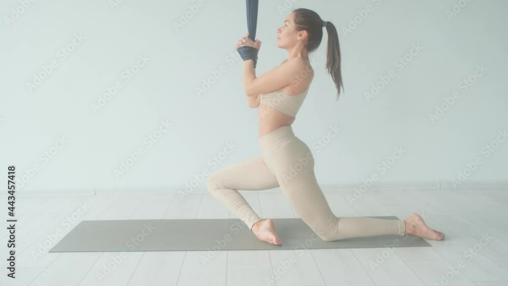 Young woman sits in lotus position in a bright room. The girl does exercises from fly yoga. Young woman sits in lotus position in a bright room. The girl does exercises from fly yoga.