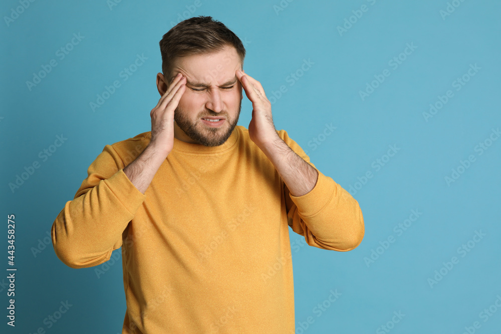 Fototapeta premium Man suffering from migraine on light blue background, space for text