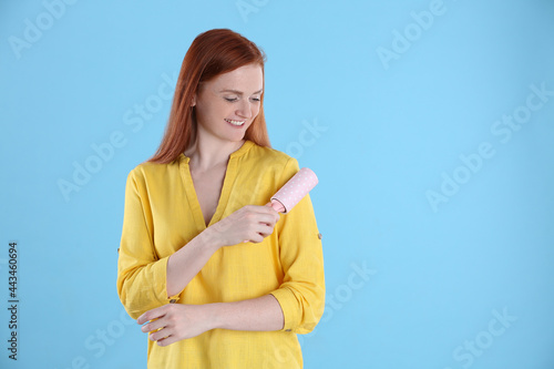 Young woman cleaning clothes with lint roller on light blue background, space for text © New Africa