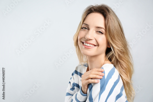 Portrait of happy young woman with beautiful blonde hair and charming smile on light background. Space for text