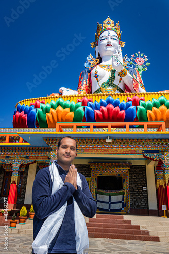 young man praying in front of buddhist colorful goddess statue with blue sky at morning photo