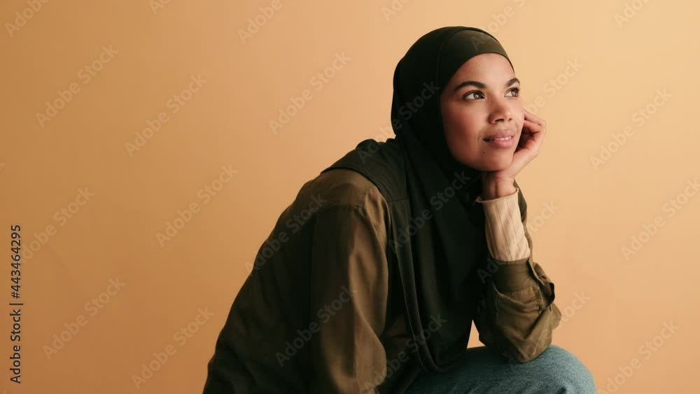 A thinking young arabian woman is looking to the side isolated over beige background A thinking young arabian woman is looking to the side isolated over beige background