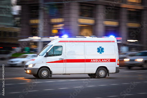 Ambulance Van on a wide city street. White emergency vehicle with warning lights and siren moving fast an avenue. Metropolis rescue services transport. Motion blur and selected focus
