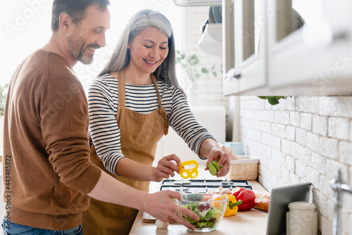 Happy mature middle-aged couple cooking vegetable vegetarian salad together in the kitchen  helping in preparation of food meal. Family moments  domestic homemade food