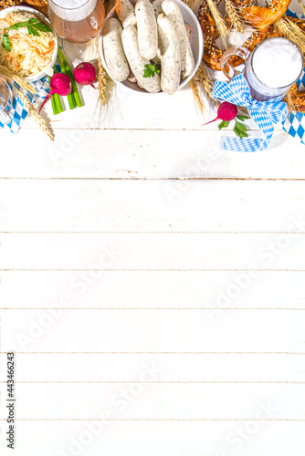 Oktoberfest food background, Traditional bavarian holiday food menu, sausages with pretzels, sauerkraut, beer glass and mugs on white wooden sun lighted background copy space