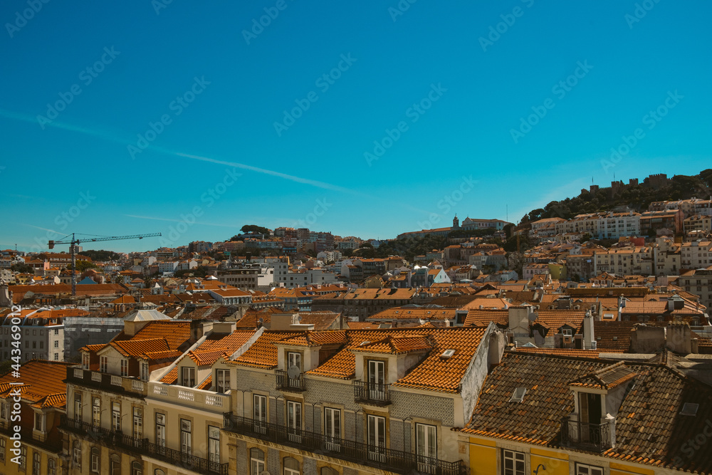 Lisbon skyline rooftop view on a sunny summer day with traditonal orange rooftops of the Alfama district with sea visible in the landscape