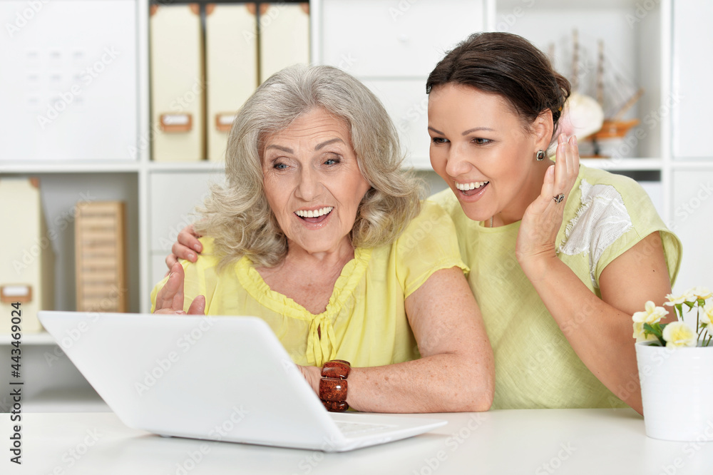 Portrait of mother and daughter sitting at table with laptop, at home Portrait of mother and daughter sitting at table with laptop, at home
