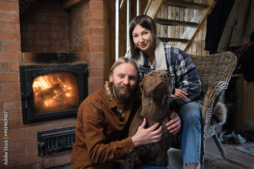 Portrait of young couple warming up near the fireplace together with their dog during cold winter evening