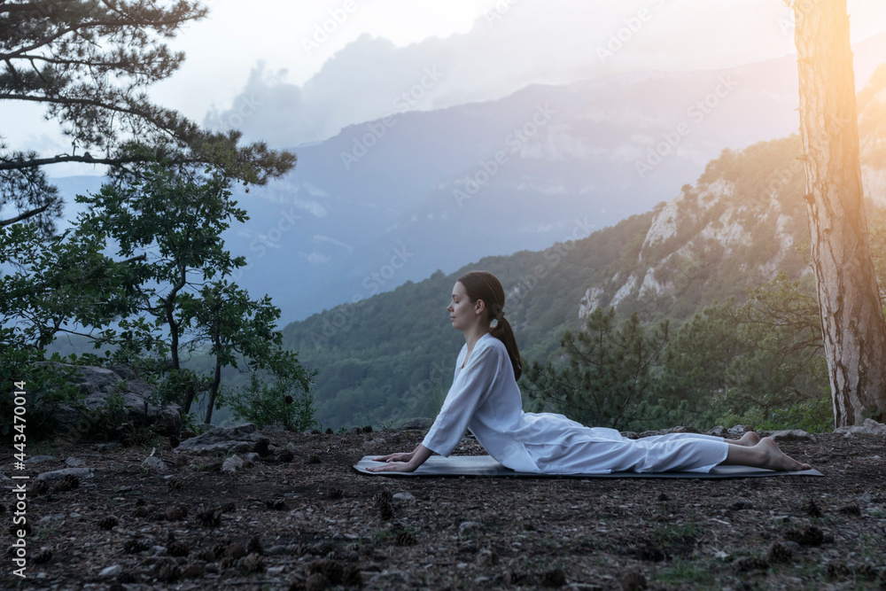 Beautiful young woman practices yoga and meditates on the mountain. Calmness and unity with nature.