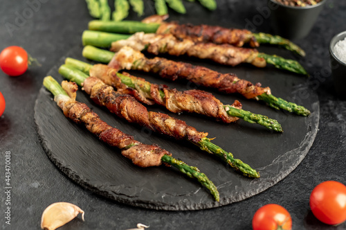 Baked asparagus with bacon and spices on a stone background