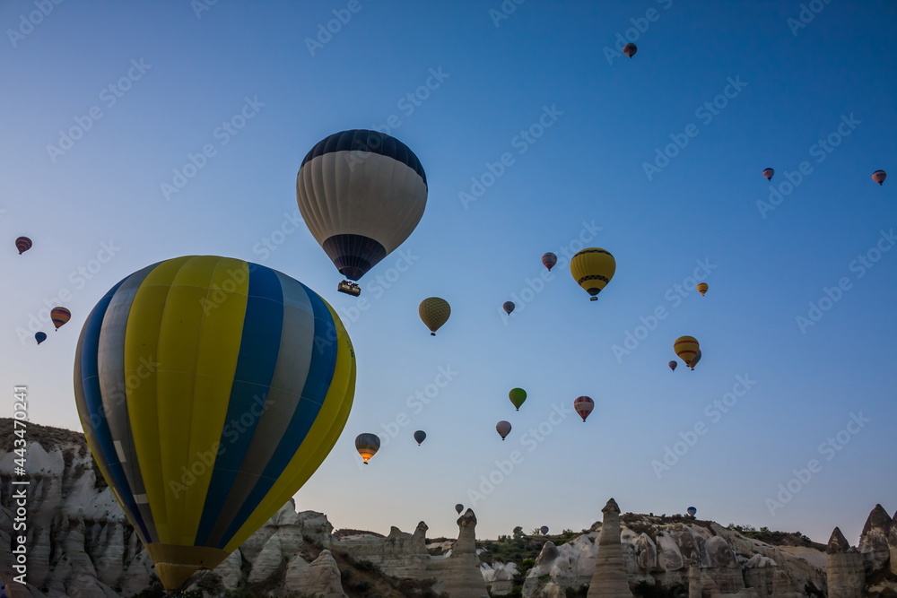 Fototapeta premium Hot air balloons flying over the valley at Cappadocia, Turkey. Goreme Balloon Festival. Beautiful hot air balloons take off at sunrise. Hot air balloons in the blue sky