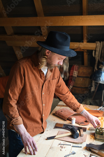 Carpenter in hat repairing the products with tools at his workplace in the workshop