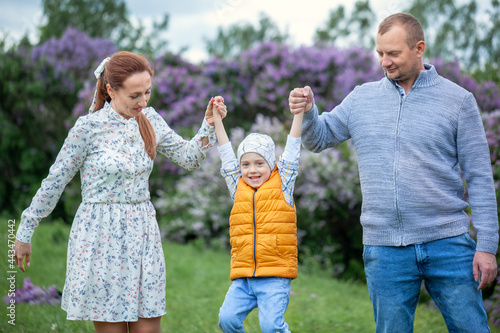 Happy family walking in the beautiful park. Parents holding the child's hands. Mom, dad and baby are happy to walk in summer day. © Volha Zaitsava