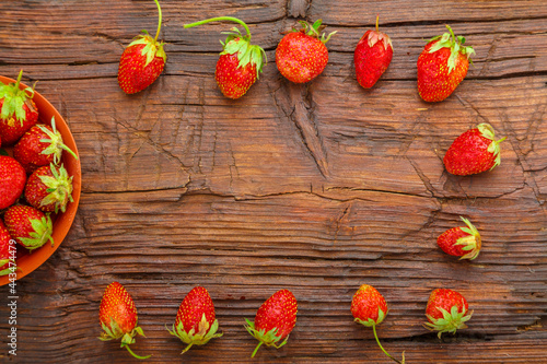 Ripe strawberries in a plate on a wooden table next to a frame.