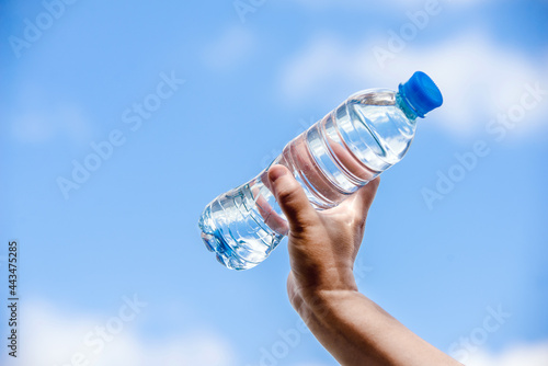 A girl holds a bottle of drinking water in her hand against a blue sky background 