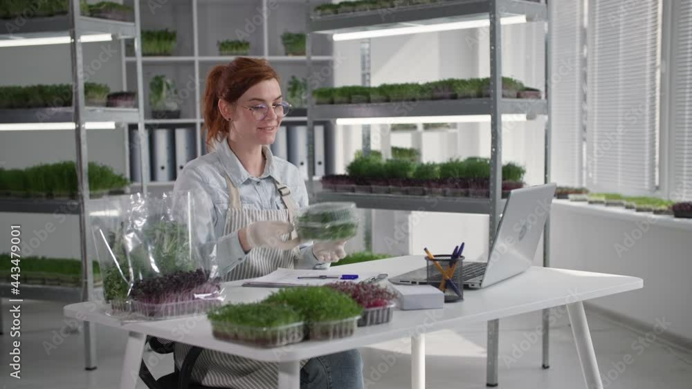 online store, charming female small business owner selling packaged micro green while video chatting with customer at table in greenhouse online store, charming female small business owner selling packaged micro green while video chatting with customer at table in greenhouse