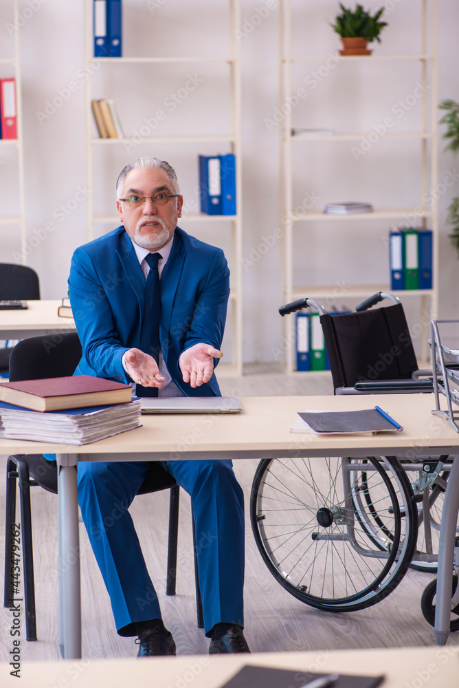 Old male employee in wheel-chair sitting in the office Old male employee in wheel-chair sitting in the office