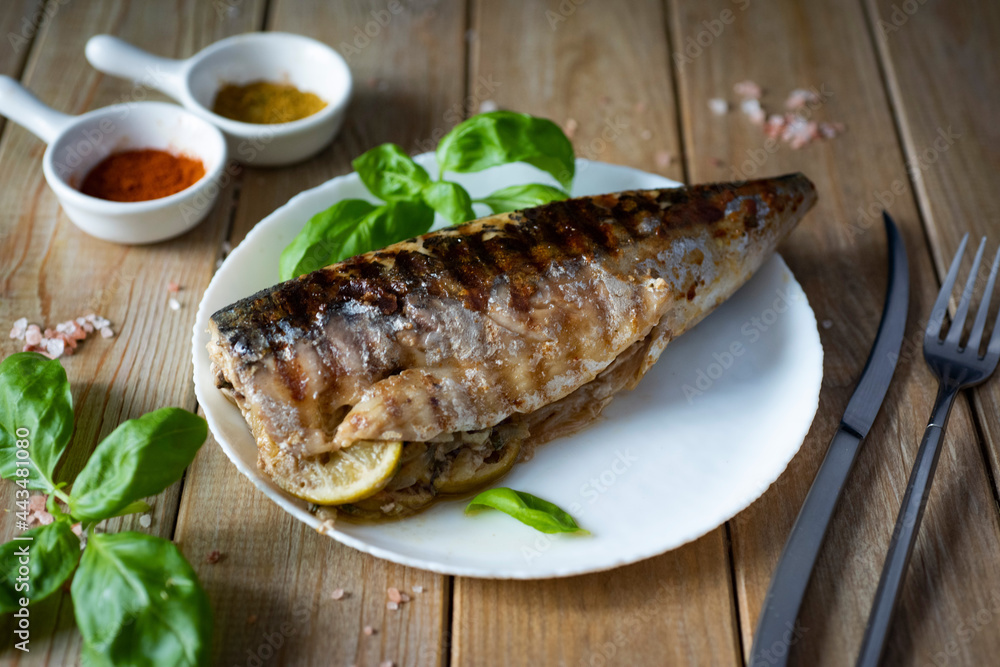 Fish lunch: grilled mackerel on a white plate on a wooden table. Fish lunch: grilled mackerel on a white plate on a wooden table.