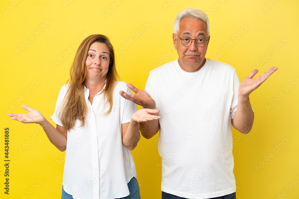 Middle age couple isolated on yellow background having doubts and with confuse face expression Middle age couple isolated on yellow background having doubts and with confuse face expression