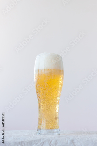A full glass of light beer with bubbles and foam stands on a white background