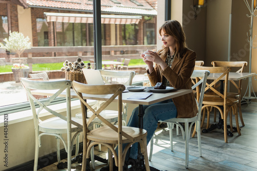 Freelancer holding cup near dessert and laptop in cafe. © LIGHTFIELD STUDIOS