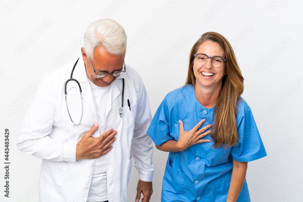 Middle age doctor and nurse isolated on white background smiling a lot while putting hands on chest Middle age doctor and nurse isolated on white background smiling a lot while putting hands on chest