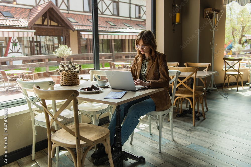 Stylish woman using laptop near dessert and coffee in cafe. Stylish woman using laptop near dessert and coffee in cafe.