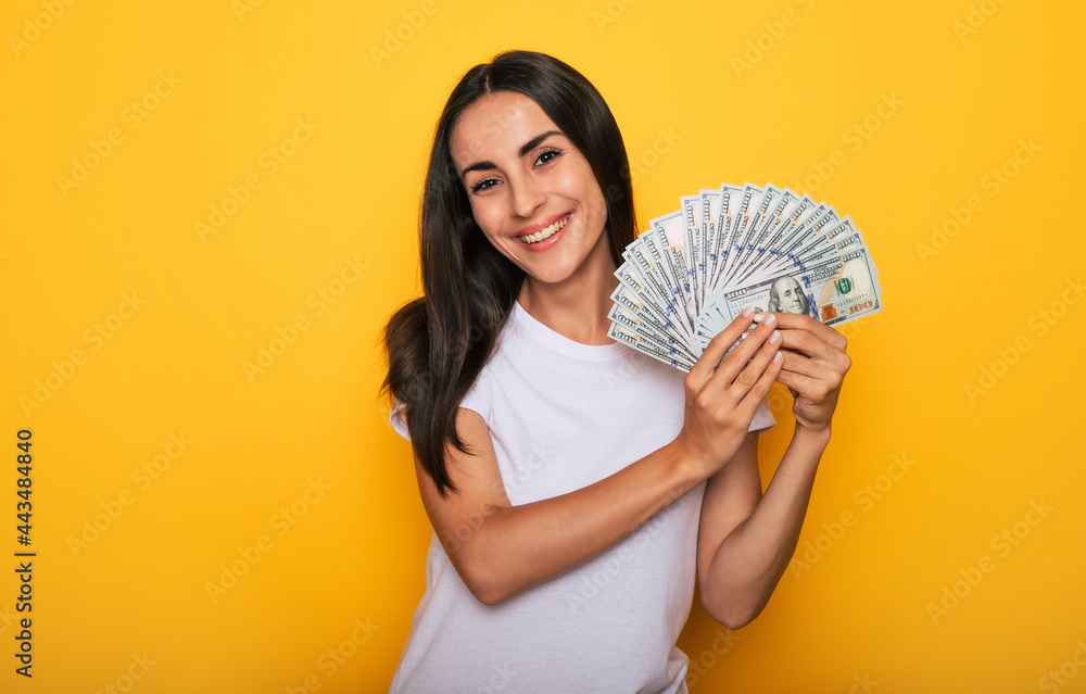 Young happy excited beautiful woman emotionally looking in the camera with a lot of money in her hands and having fun isolated on yellow background Young happy excited beautiful woman emotionally looking in the camera with a lot of money in her hands and having fun isolated on yellow background