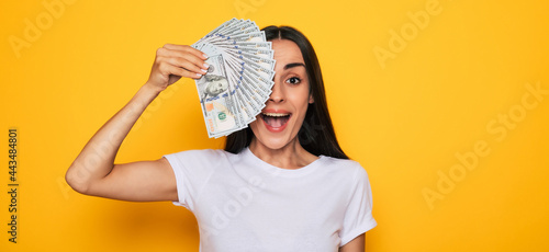 Young happy excited beautiful woman emotionally looking in the camera with a lot of money in her hands and having fun isolated on yellow background