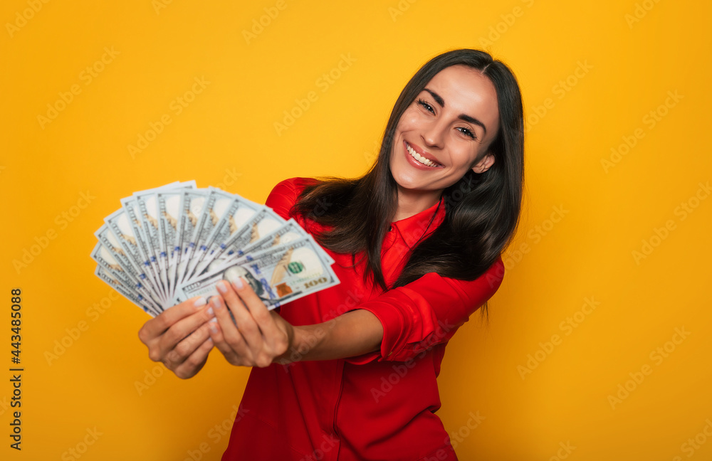 Young happy excited beautiful woman emotionally looking in the camera with a lot of money in her hands and having fun isolated on yellow background Young happy excited beautiful woman emotionally looking in the camera with a lot of money in her hands and having fun isolated on yellow background