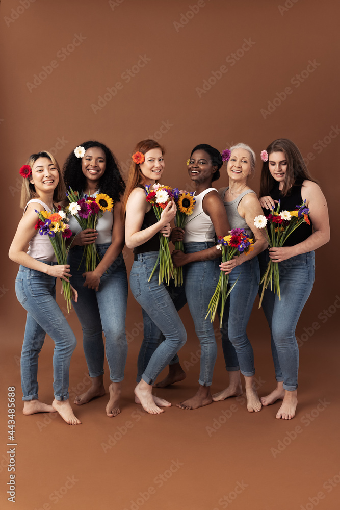 Obraz premium Full body shot of six women of different ages standing together with bouquets of flowers. Smiling women in casuals with flowers in hair.