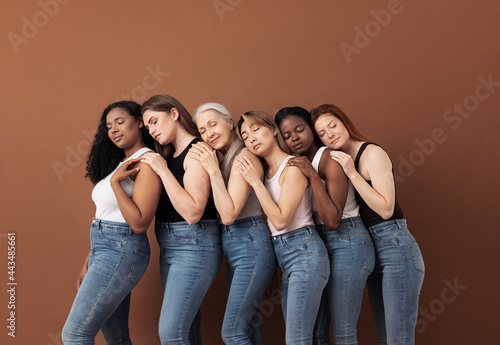 Diverse women in casuals embracing each other while standing with closed eyes over brown background