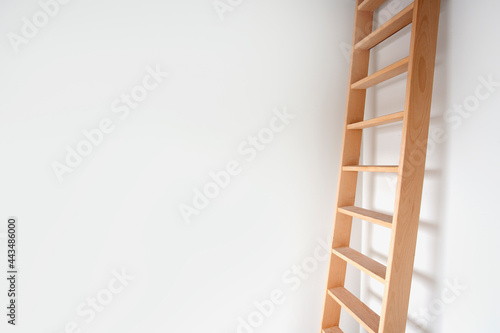 Sideview of a wooden ladder leaning against white wall modern design, stylish stairs in bright room with copy space