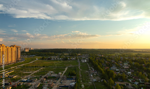 Panorama of the outskirts from the megalopolis under construction at sunset. Multistorey buildings are being converted into construction and wooden houses.