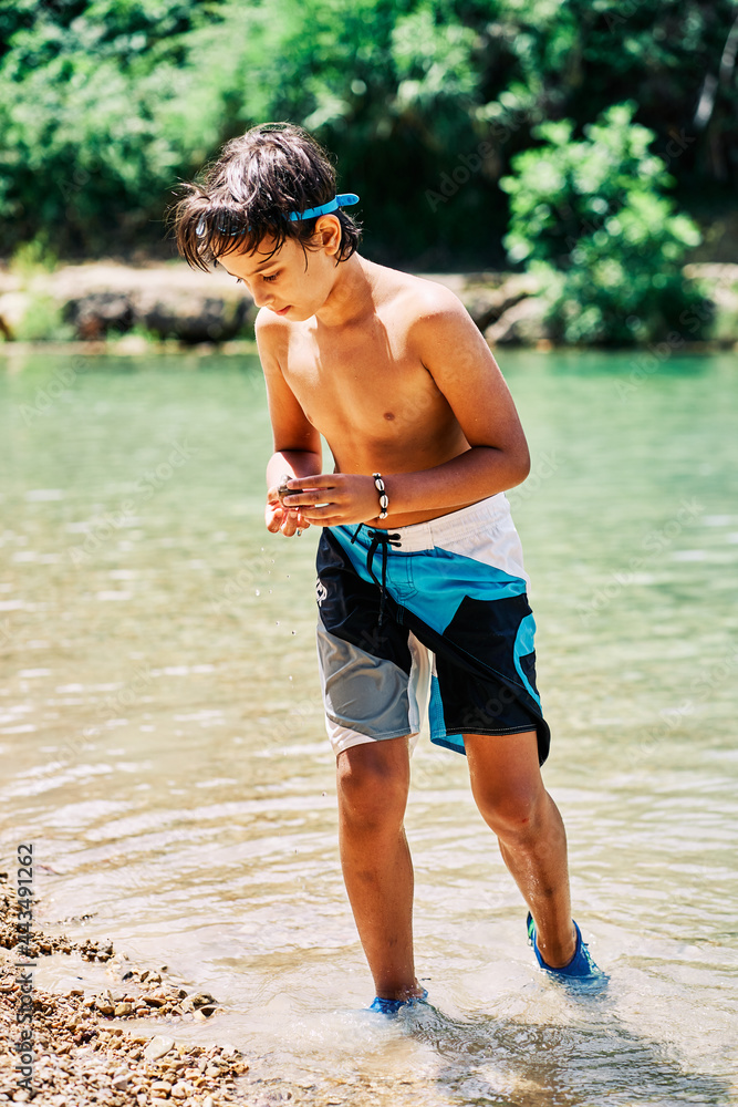 Caucasian boy in swimming trunks into the river water in summer Caucasian boy in swimming trunks into the river water in summer