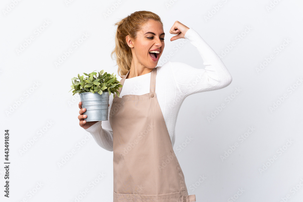 Young blonde gardener woman girl holding a plant over isolated white background celebrating a victory