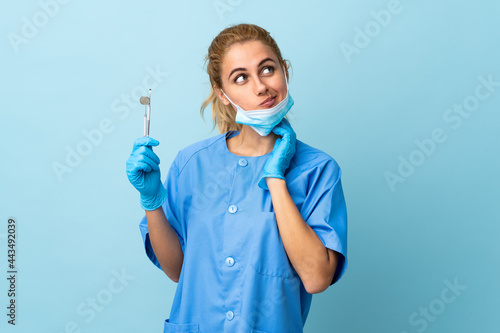 Young woman dentist holding tools over isolated blue background thinking an idea
