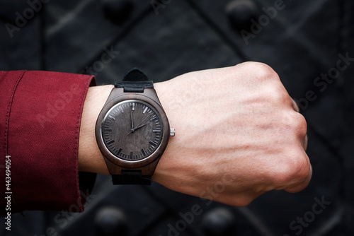 Brown wooden wrist watch with a leather strap on a man's wrist on a black background. Close-up. Space for text. High quality photo