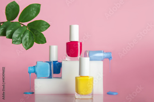 Cosmetic nail polishes on trendy podium. Red, blue and yellow gel polish on pink background with natural leaves. Top view.