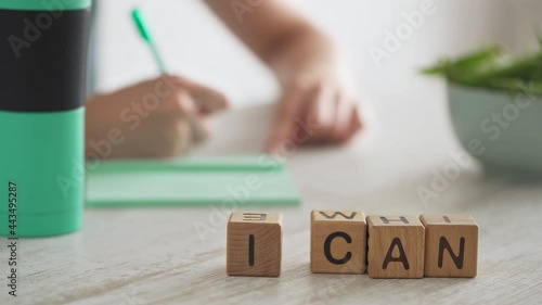 Phrase I can laid out from cubes on table in foreground. In background girl writes in notebook. Developing plan to achieve goal. Healthy lifestyle and self-improvement Motivation to achieve the goal
