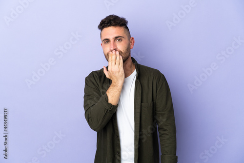 Caucasian man isolated on purple background covering mouth with hand