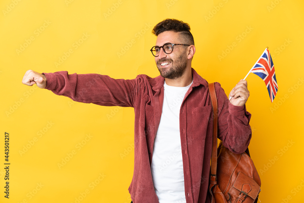 Caucasian man holding an United Kingdom flag isolated on yellow background giving a thumbs up gesture Caucasian man holding an United Kingdom flag isolated on yellow background giving a thumbs up gesture