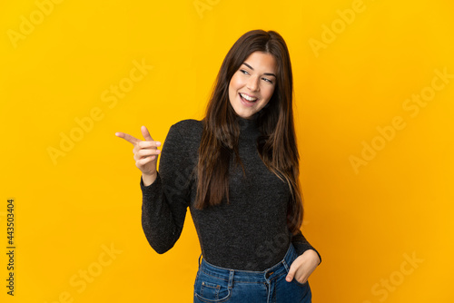 Teenager Brazilian girl isolated on yellow background pointing finger to the side and presenting a product